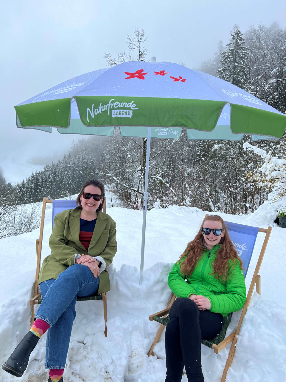 Zwei junge Damen in Liegestühlen und mit Sonnenschirm im Schnee
